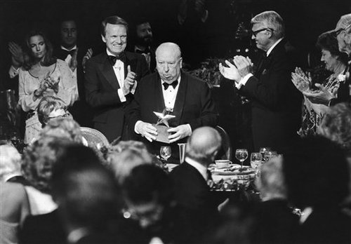 American Film Institute Award and producer and director Alfred Hitchcock, center, stands to receive the applause of producer George Stevens Jr., left, and actor Cary Grant at the Institutes testimonial dinner in Beverly Hills, California, United States, on Wednesday, March 8, 1979. Hitchcock received the Seventh Annual Life Achievement Award in a 90-minute tribute to the veteran film maker. (AP Photo/Huynh Thanh My)